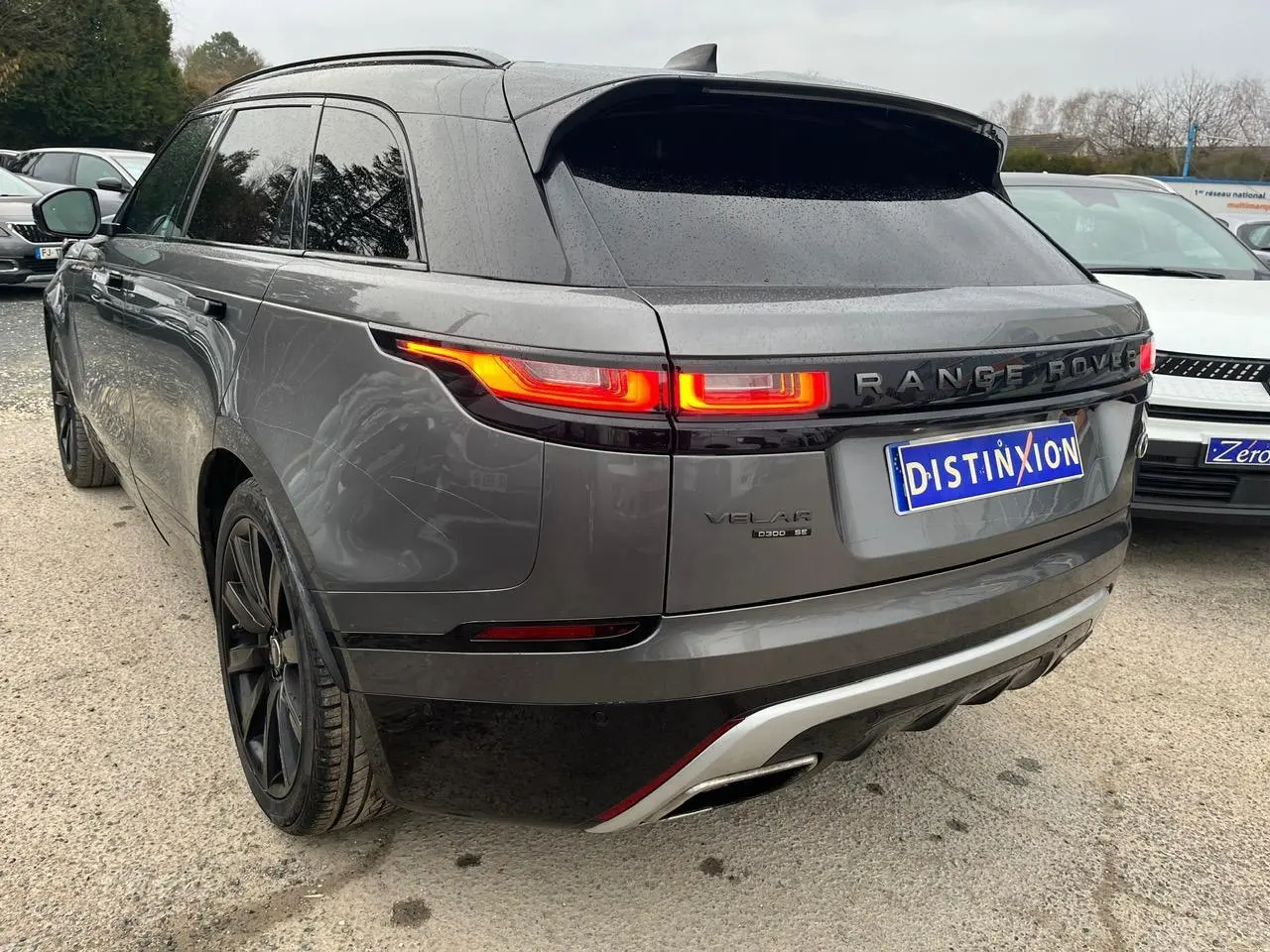 Vue 3/4 arrière droite d’un Range Rover Velar gris ammonite avec jantes noires 21 pouces et feux arrière allumés.