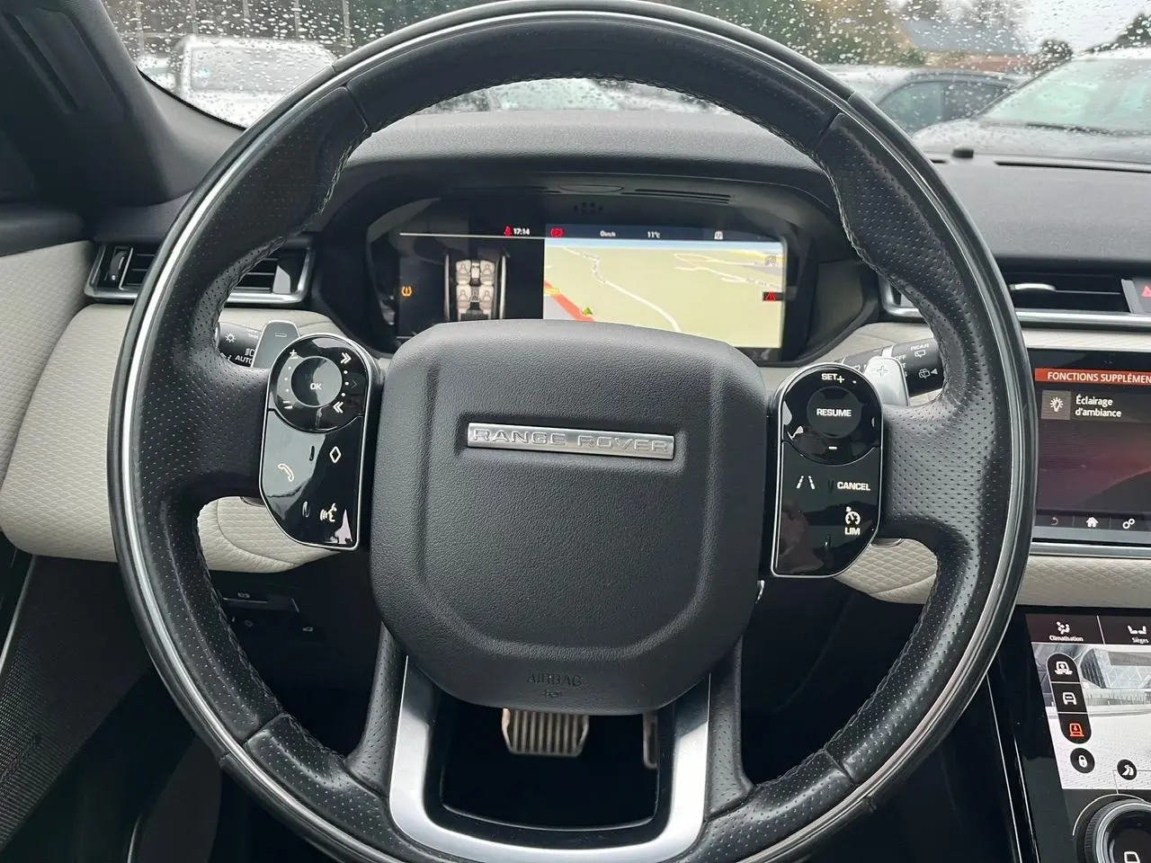 Vue rapprochée du volant cuir perforé noir du Range Rover Velar avec commandes intégrées et écran de navigation digital.
