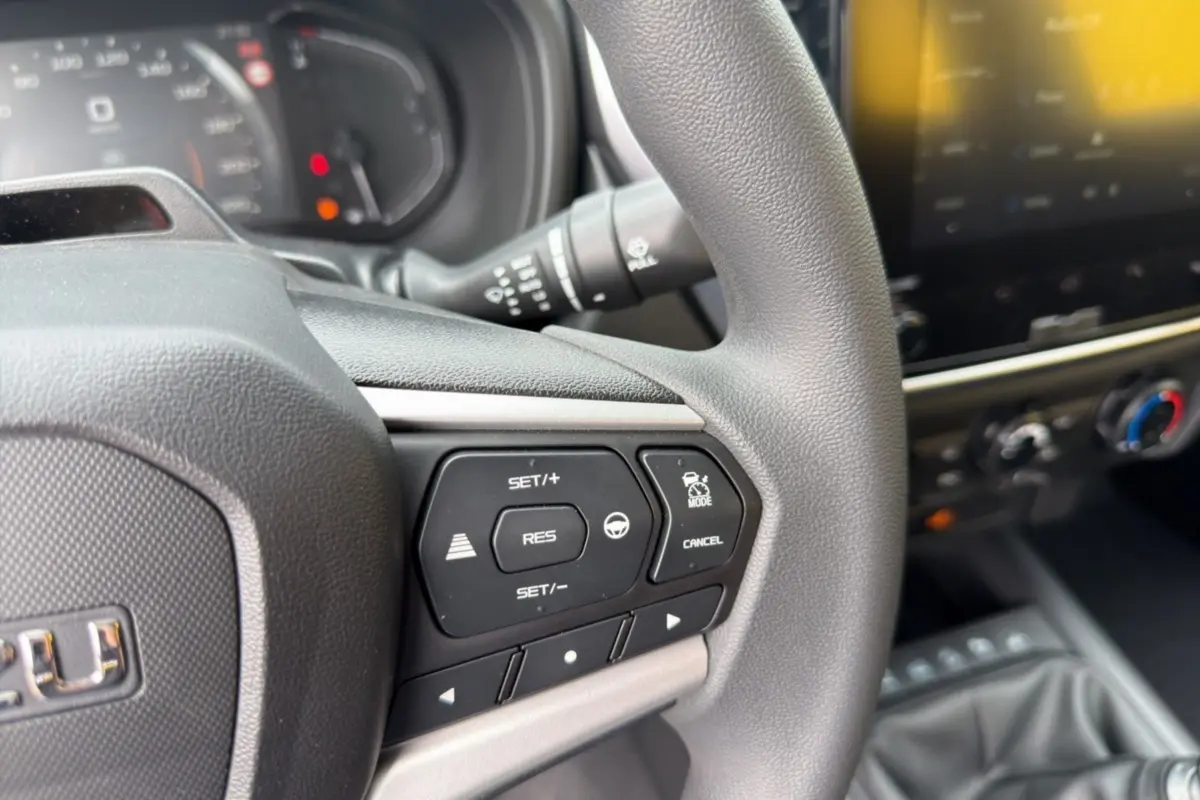 Gros plan sur le volant multifonctions gris foncé de l'Isuzu D-MAX 2026 avec commandes de régulateur et tableau de bord flou.