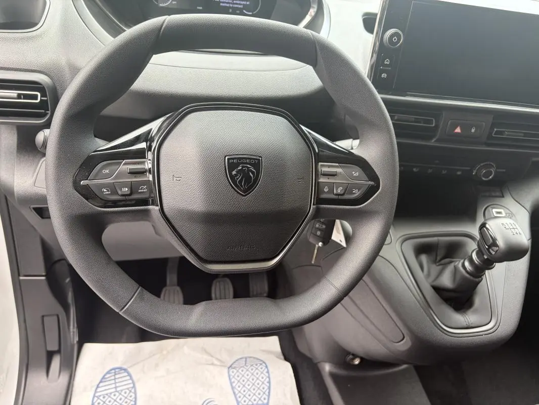 Vue intérieure centrée sur le volant cuir multifonctions et levier de vitesses manuel du Peugeot Partner blanc 2026.