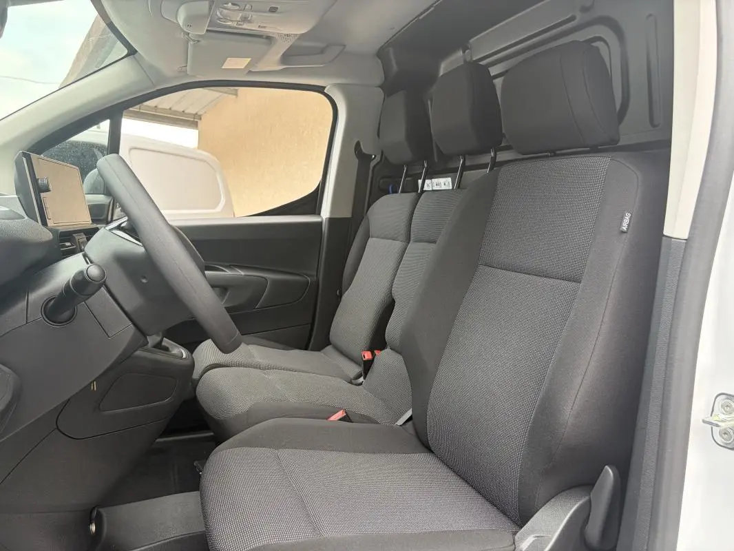Vue intérieure côté conducteur du Peugeot Partner blanc 2026, montrant les sièges tissu gris et le volant multifonctions.