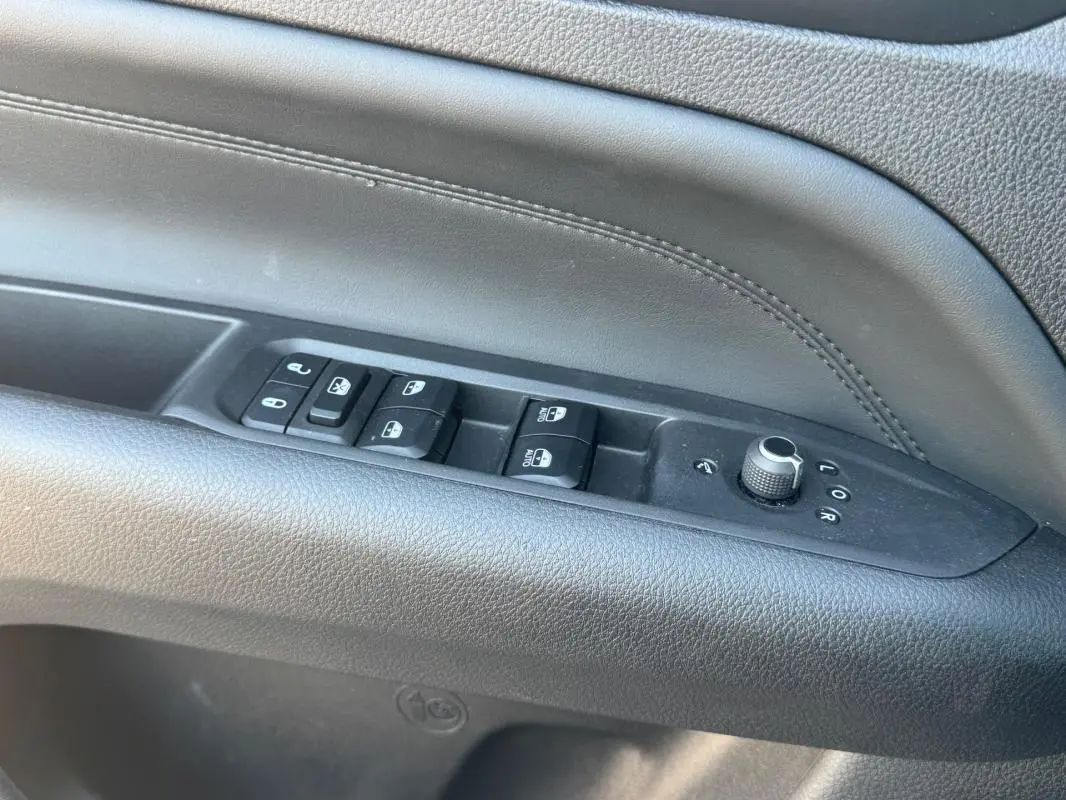 Gros plan sur les commandes de lève-vitres et réglages des rétroviseurs sur la porte intérieure noire du Jeep Compass 2025.