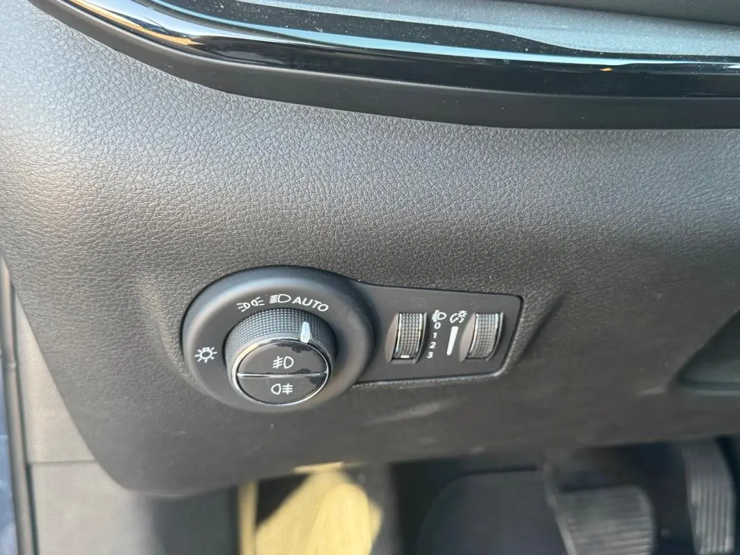 Gros plan sur les commandes d’éclairage du tableau de bord du Jeep Compass bleu, avec molette de réglage des phares et boutons adjacents.