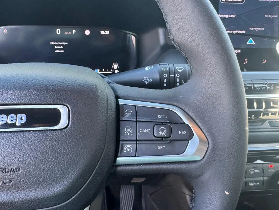 Gros plan sur le volant noir du Jeep Compass 2025 avec commandes au volant et tableau de bord numérique en arrière-plan.
