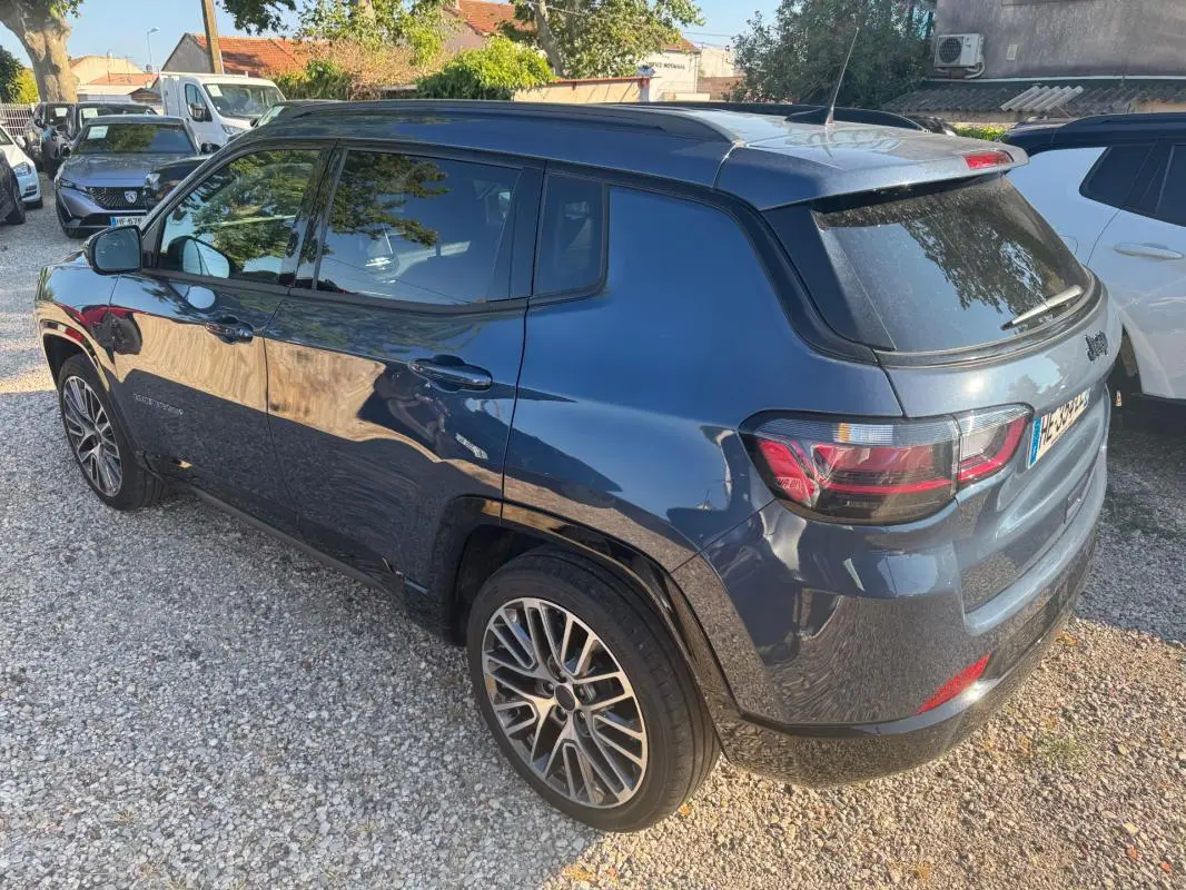 Jeep Compass bleu vue 3/4 arrière côté gauche, avec jantes alliage 19 pouces et barres de toit visibles.