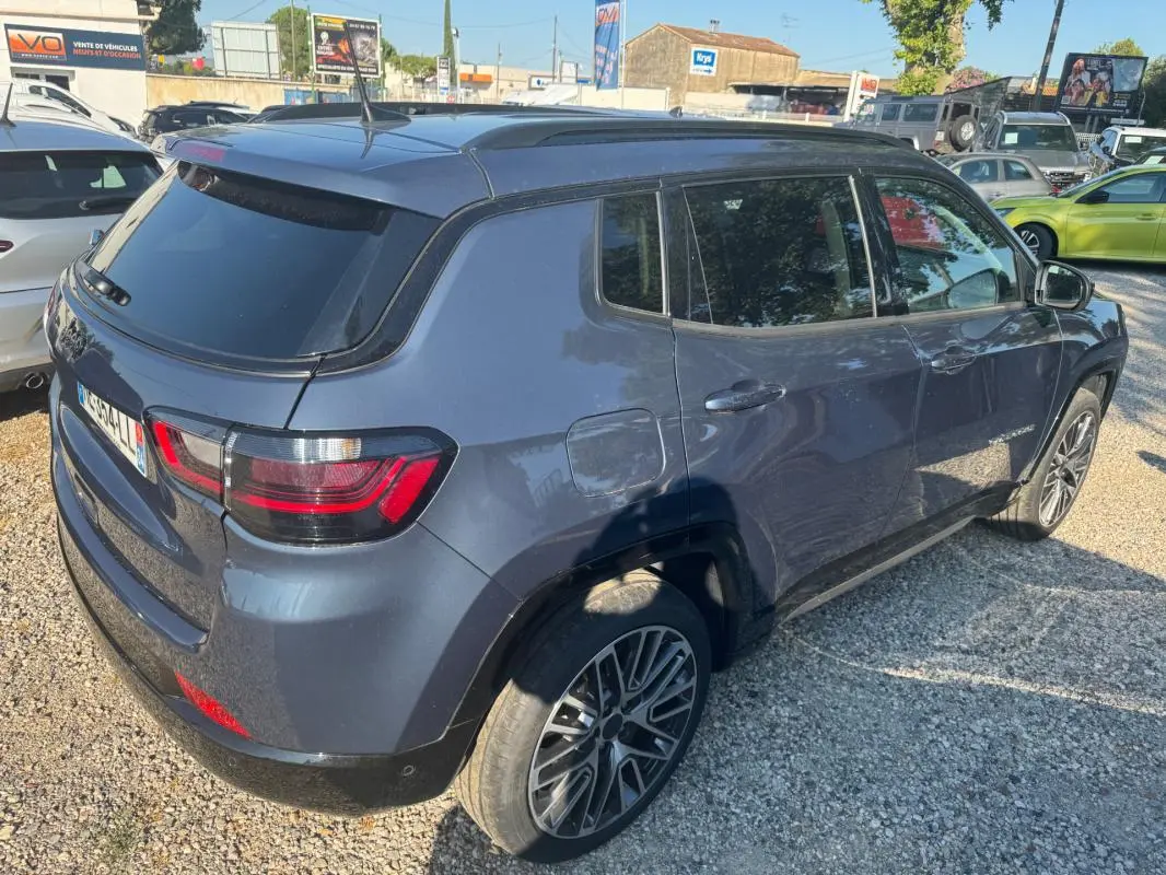 Jeep Compass bleu en 3/4 arrière droit, avec jantes alliage 19 pouces et barres de toit visibles.
