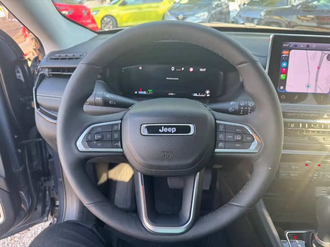 Vue intérieure centrée sur le volant Jeep noir du Compass 2025 avec tableau de bord numérique et écran tactile visible.