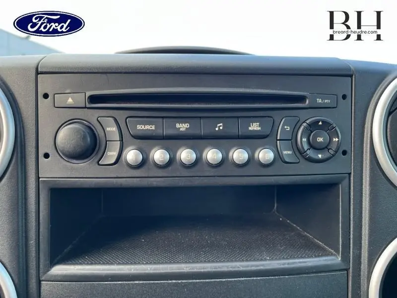 Vue rapprochée de la console centrale noire du Citroën Berlingo blanc, mettant en valeur la radio et les commandes audio.