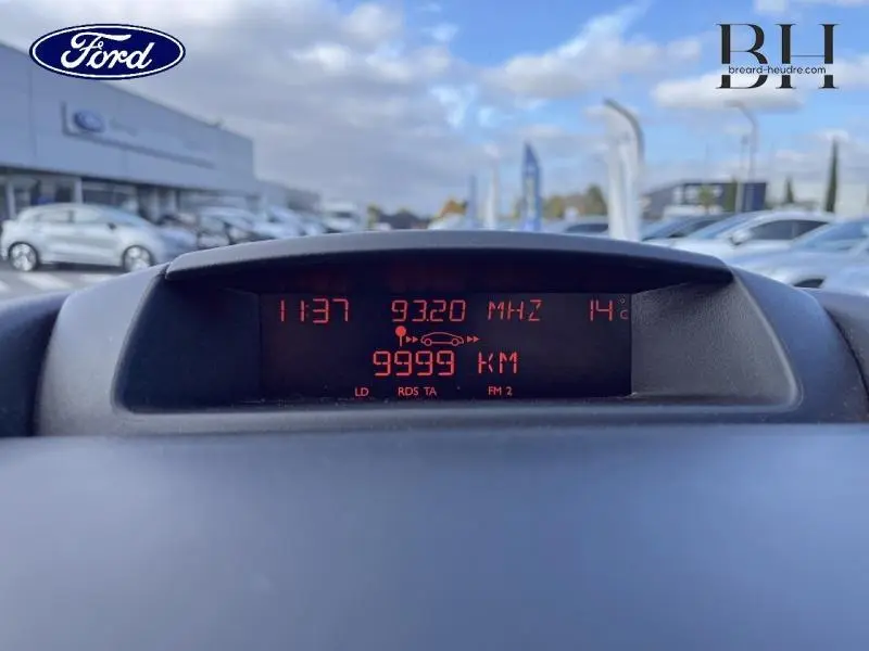 Affichage digital du tableau de bord du Citroën Berlingo blanc, montrant la radio et le compteur kilométrique à 9999 km.