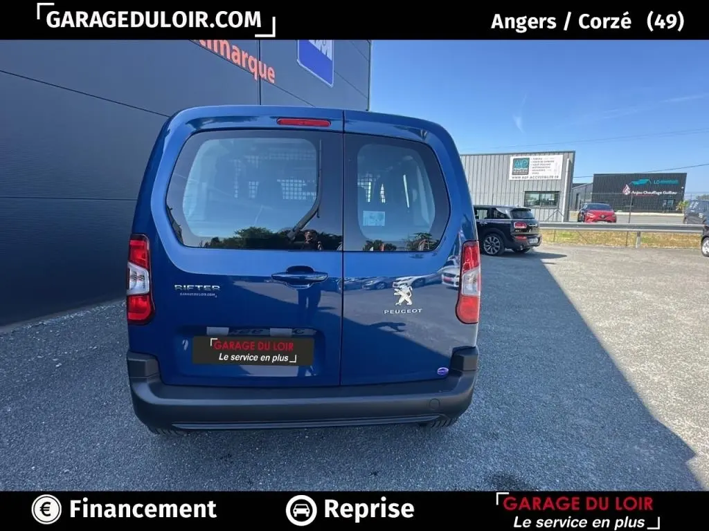 Vue arrière du Peugeot Rifter bleu 2024 avec portes battantes et logo visible sur un parking extérieur.