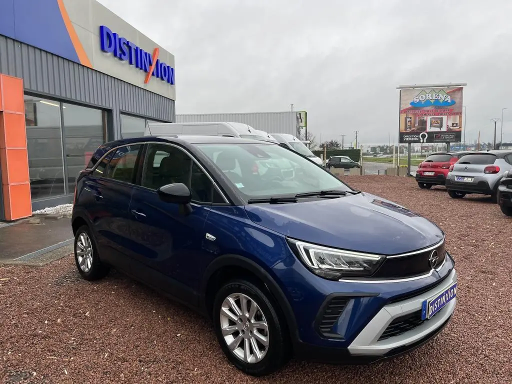 Opel Crossland X bleu clair en 3/4 avant droit avec toit noir, stationné devant un bâtiment commercial.