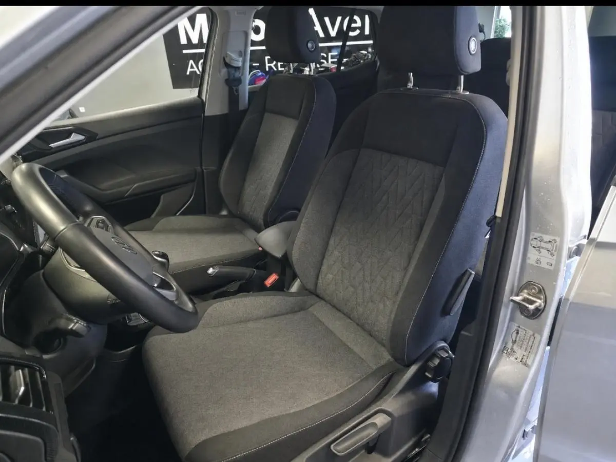 Vue intérieure côté conducteur du Volkswagen T-Cross gris 2025, montrant les sièges avant en tissu et le volant multifonction en cuir.