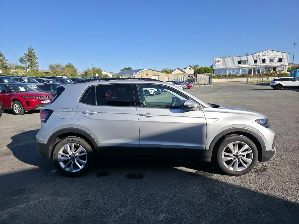 Vue de profil côté gauche d'un Volkswagen T-Cross gris métallisé avec jantes alliage 17 pouces sur parking.
