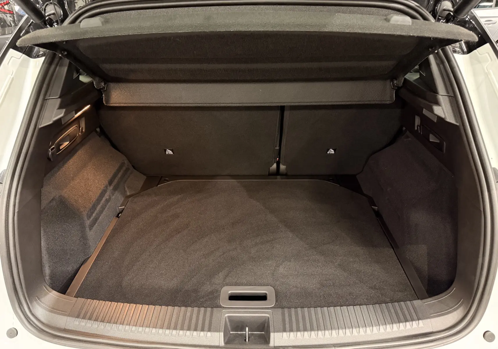Coffre ouvert vu de l'arrière d'un Renault Austral blanc nacré avec intérieur de coffre noir et cache-bagages déployé.