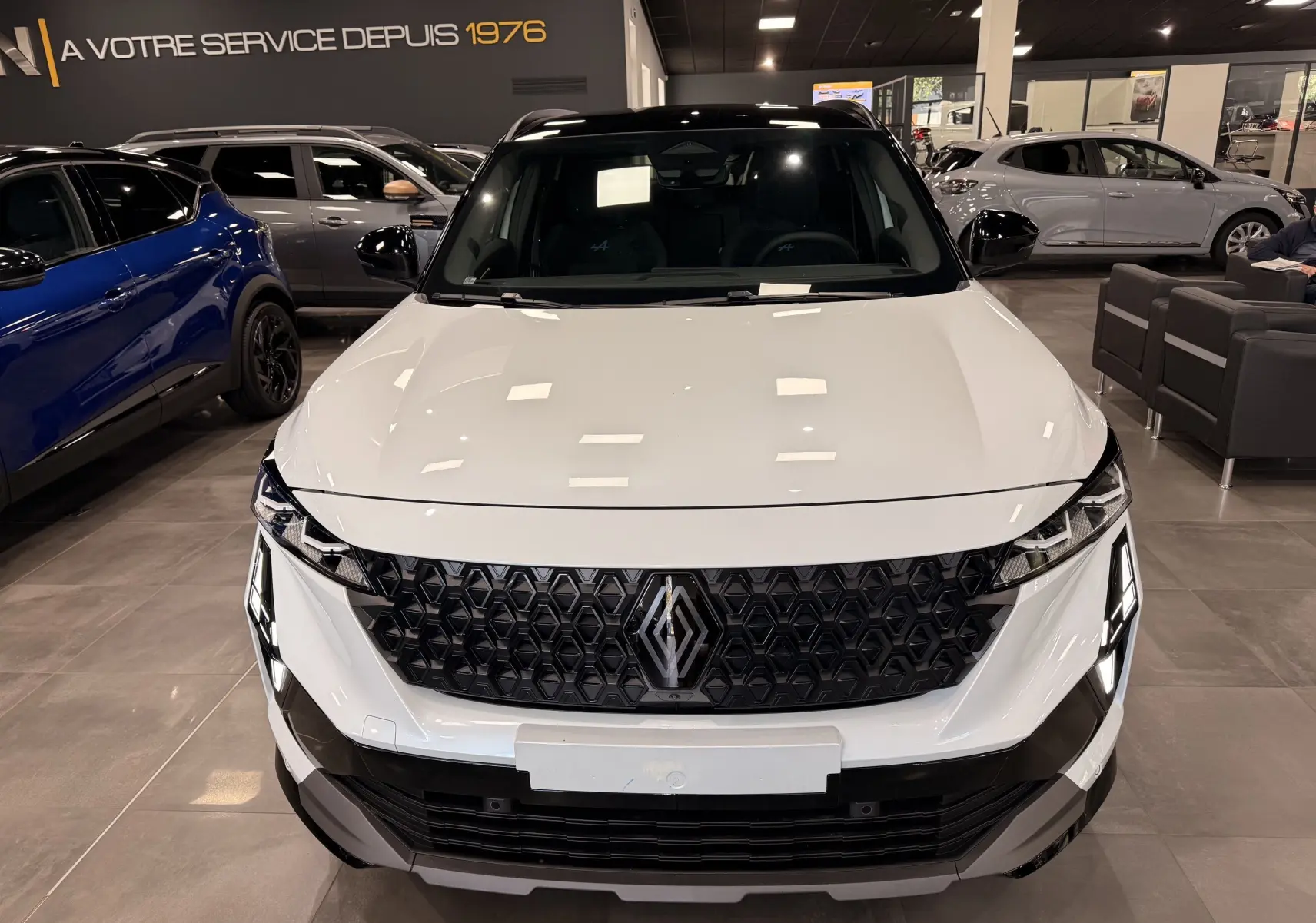 Vue de face du Renault Austral blanc nacré avec toit noir, mettant en valeur sa calandre hexagonale distinctive en showroom.