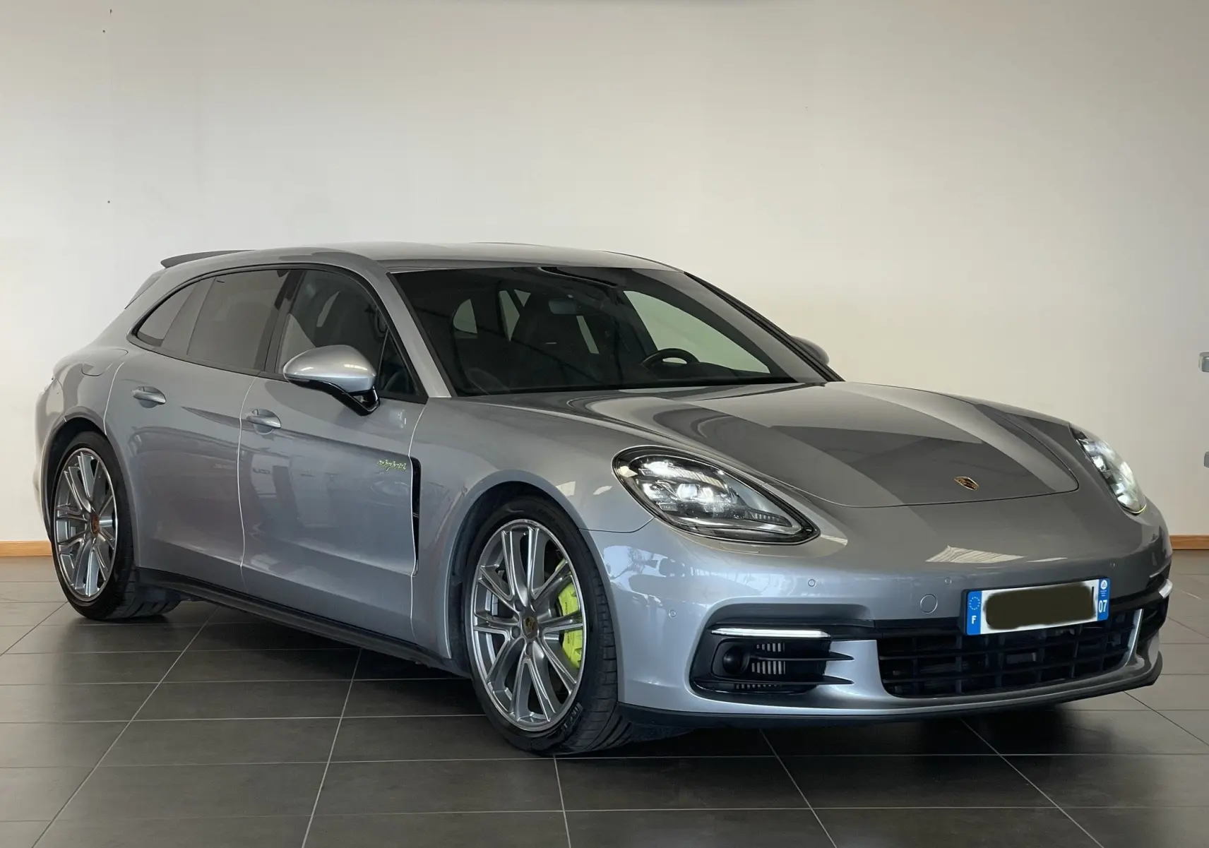 Porsche Panamera Sport Turismo gris en 3/4 avant gauche, avec jantes alliage et étriers de frein verts hybrides visibles.