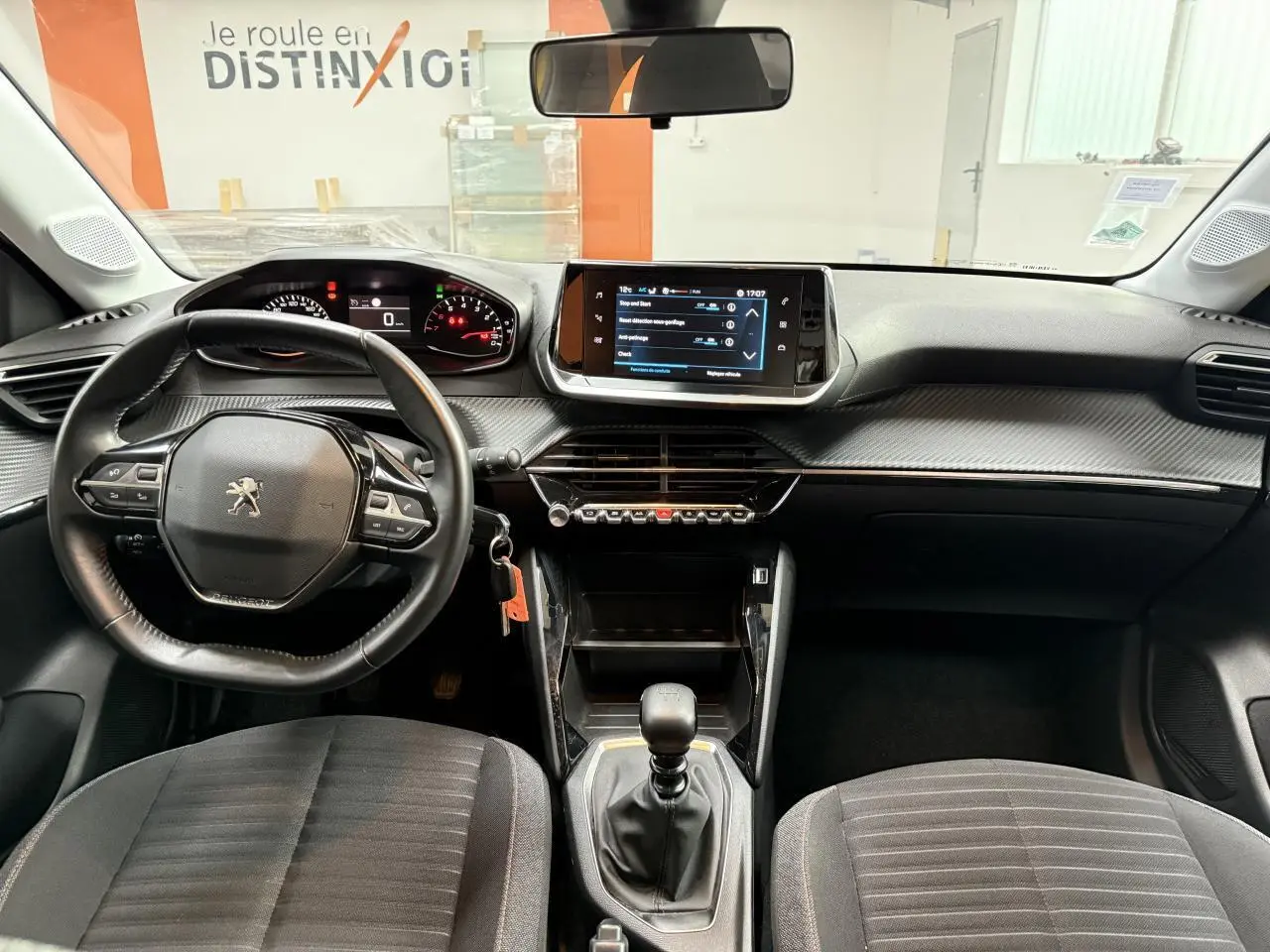Vue intérieure avant de la Peugeot 208 2020 avec tableau de bord noir, volant multifonction et écran tactile central.