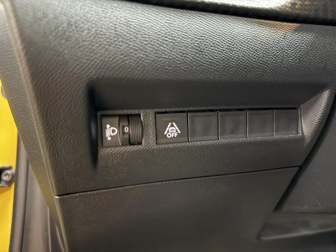 Gros plan sur les commandes de réglage des phares et de l'alerte de franchissement de ligne dans une Peugeot 208 jaune clair.