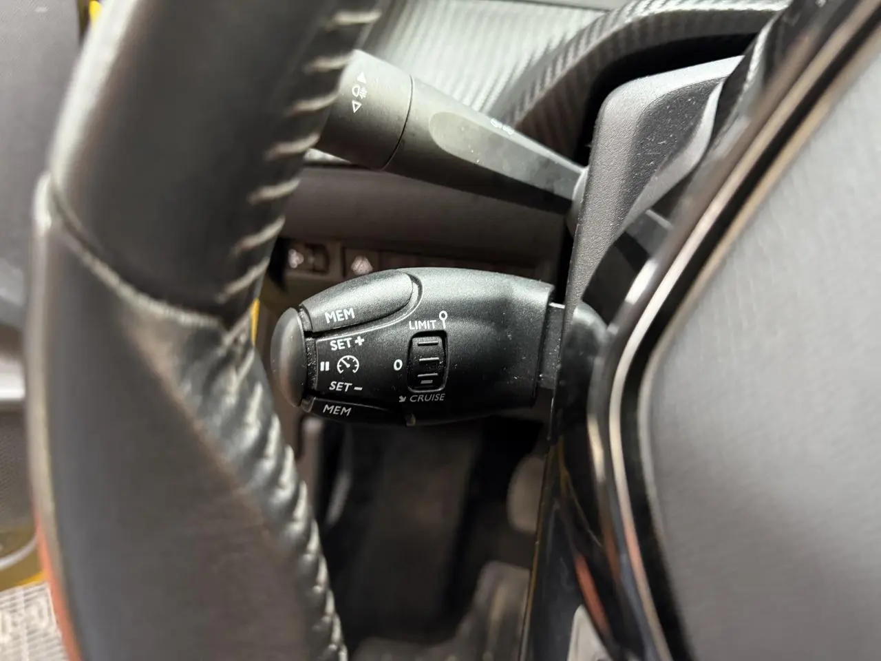 Gros plan sur la commande de régulateur de vitesse derrière le volant d'une Peugeot 208 essence jaune clair.