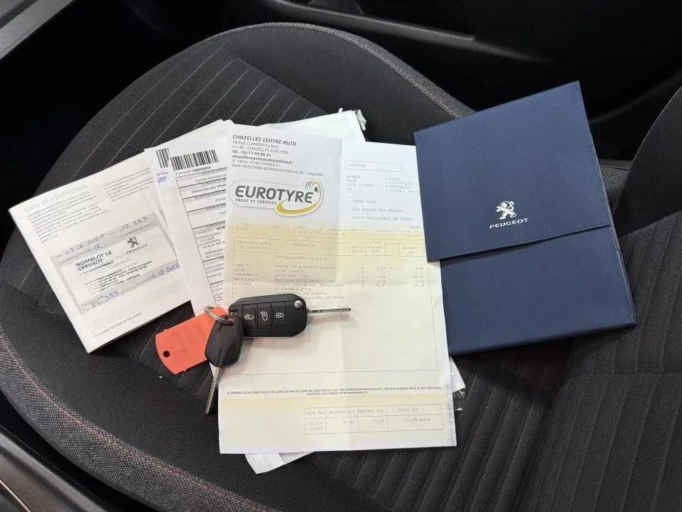 Vue rapprochée de la banquette arrière noire d'une Peugeot 208 avec clés, documents et carnet d'entretien posés dessus.