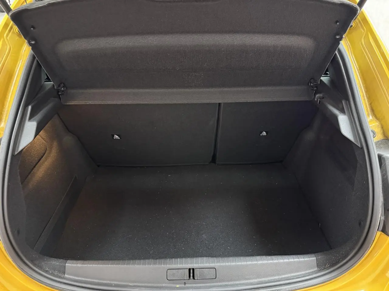 Coffre ouvert vu de l'arrière d'une Peugeot 208 jaune clair, montrant l'espace de chargement vide et les garnitures noires.