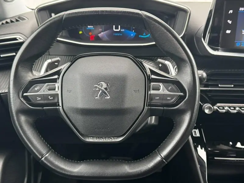 Vue rapprochée du volant multifonction noir avec logo Peugeot, tableau de bord digital et partie centrale de la console du Peugeot 2008.