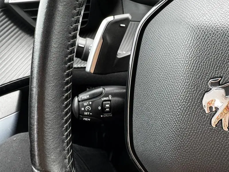 Gros plan sur le volant cuir noir de la Peugeot 2008 2020 avec logo lion argenté et commandes de régulateur de vitesse.