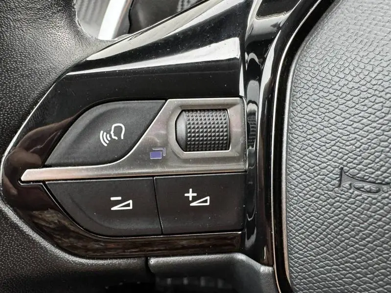 Gros plan sur les commandes vocales et volume du volant multifonction noir du Peugeot 2008 blanc banquise 2020.