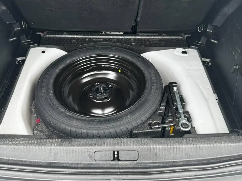 Vue plongeante sur la roue de secours noire et les outils dans le coffre blanc banquise du Peugeot 2008 2020.