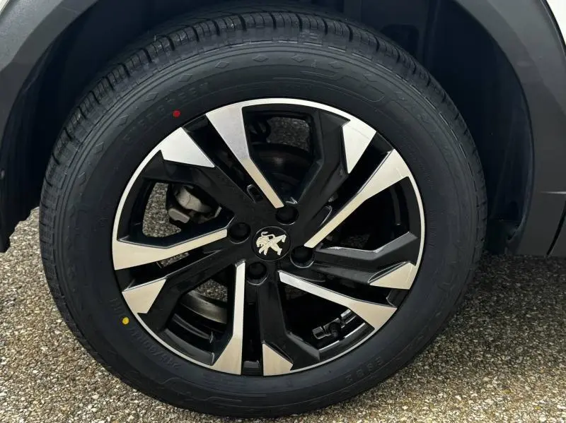 Gros plan sur la jante alu noire et argentée avec logo Peugeot d'un Peugeot 2008 blanc banquise, roue avant droite.