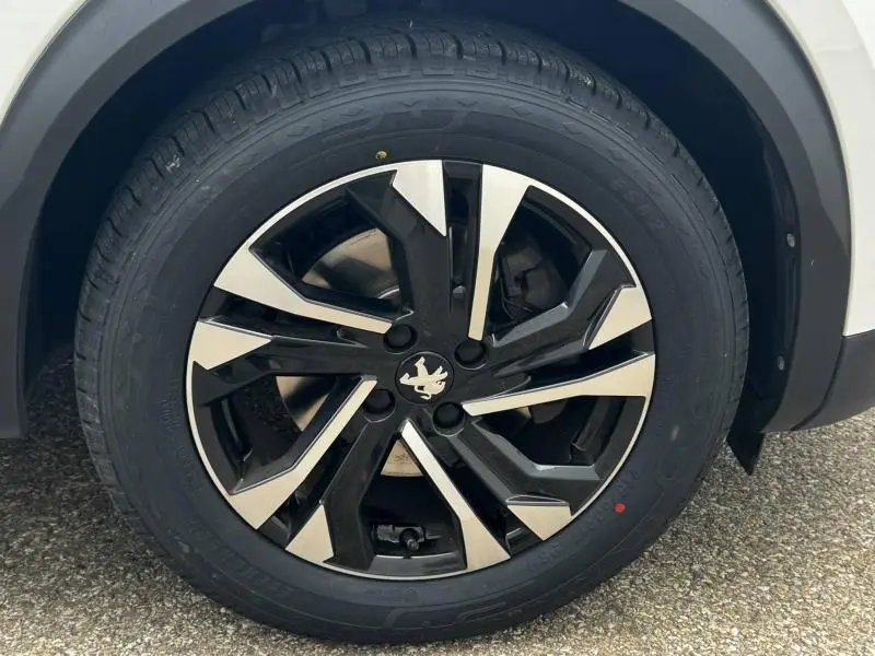 Gros plan sur la jante alu noire et argentée avec logo Peugeot d'un Peugeot 2008 blanc banquise, roue avant droite visible.
