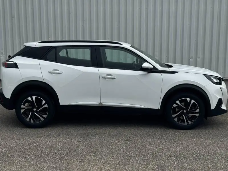 Peugeot 2008 blanc banquise vue de profil côté gauche, avec jantes alu et barres de toit noires.