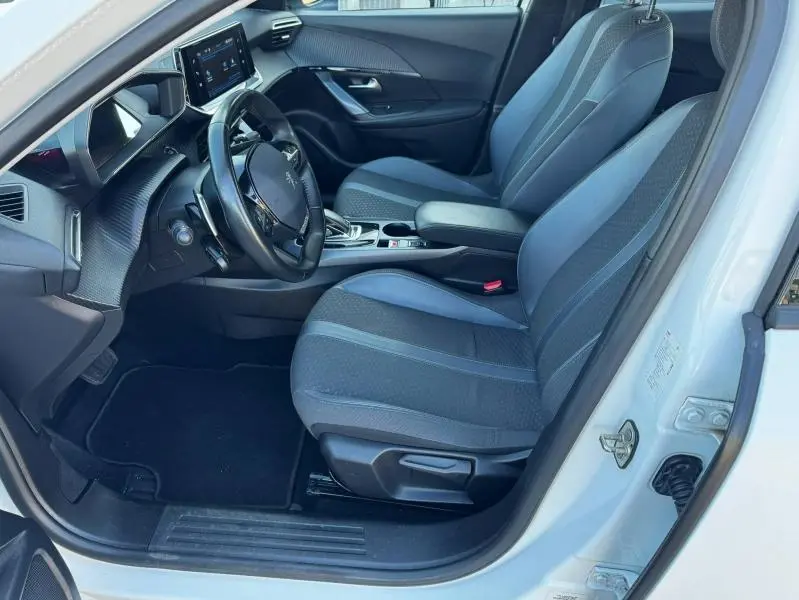 Vue intérieure côté conducteur du Peugeot 2008 blanc banquise, sièges tissu bicolore et tableau de bord moderne avec écran tactile.