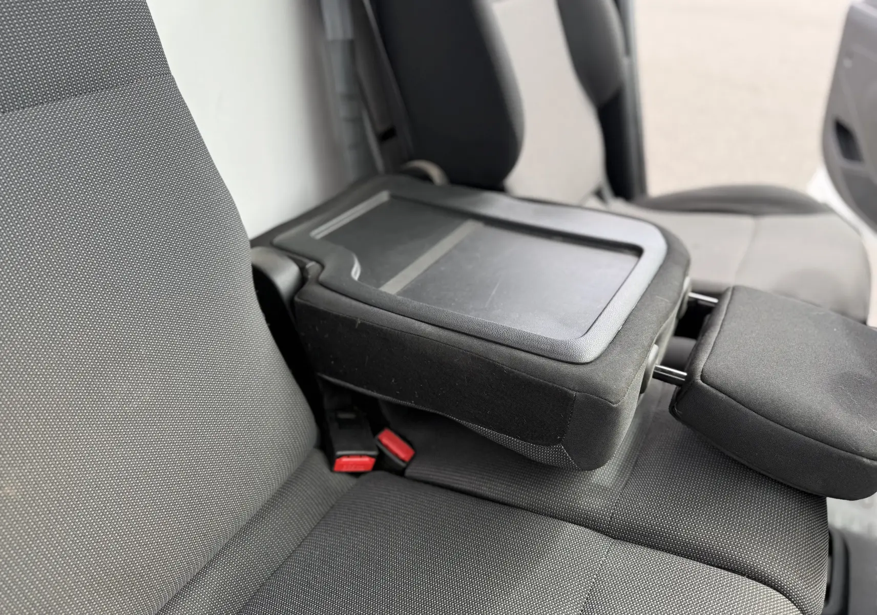 Gros plan sur les sièges avant gris foncé du Peugeot Partner 1.5 HDI 75 avec accoudoir central relevé.