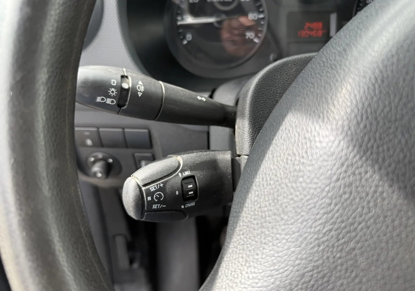 Gros plan sur le volant et les commandes de régulateur de vitesse du Peugeot Partner blanc, version 2017, intérieur tissu noir.