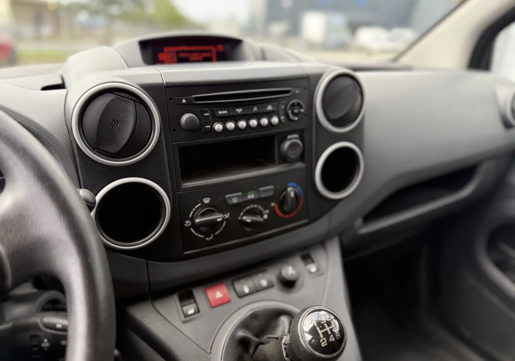 Vue rapprochée de l’intérieur du Peugeot Partner 2017, montrant la console centrale noire avec la radio et le levier de vitesse manuel.