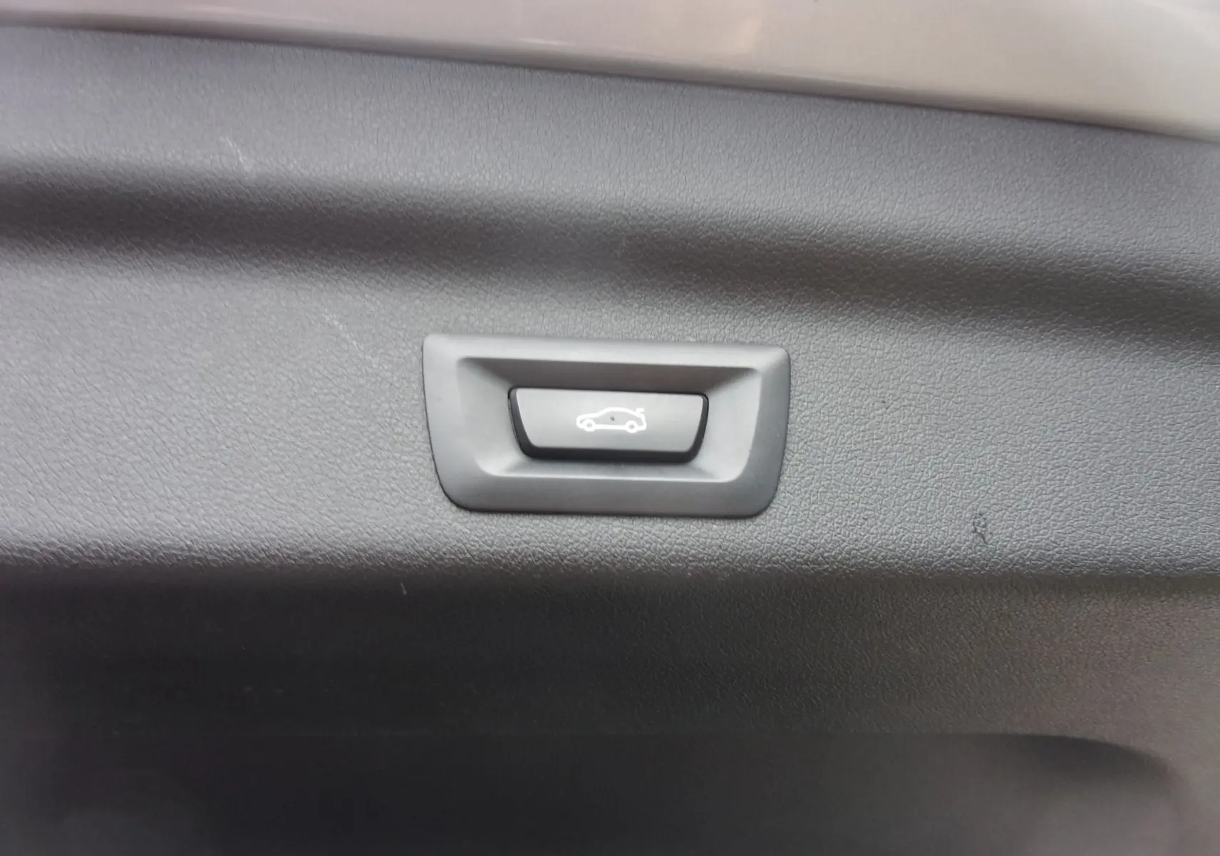 Bouton d'ouverture électrique du coffre sur panneau intérieur noir d'un BMW X1 argent métallisé 2024.