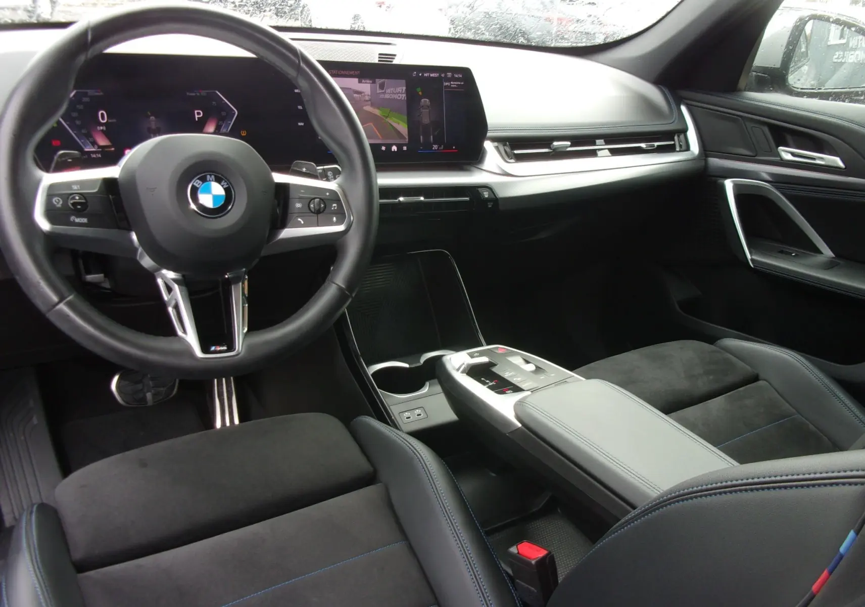 Vue intérieure du poste de conduite du BMW X1 2024 M Sport, avec volant cuir noir et écran central tactile moderne.