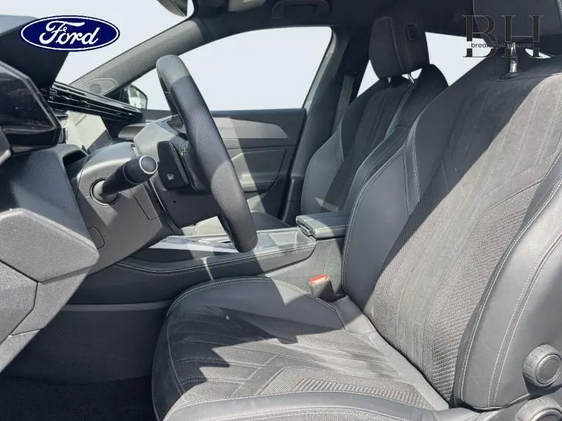Vue intérieure côté conducteur montrant les sièges en tissu noir et le volant multifonction d'une Peugeot 308 SW PHEV 2023.