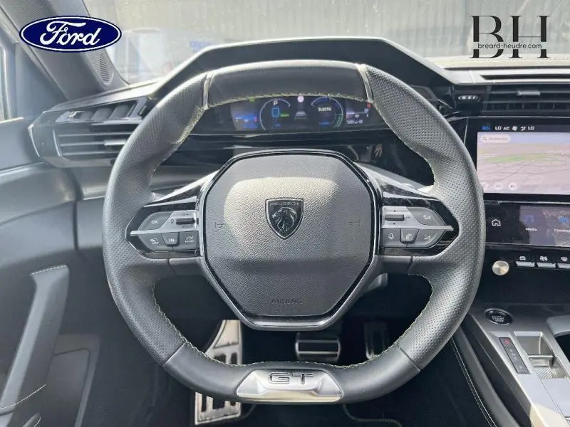 Vue rapprochée du volant GT de la Peugeot 308 SW PHEV 180ch blanc Okénite avec tableau de bord numérique et écran tactile.