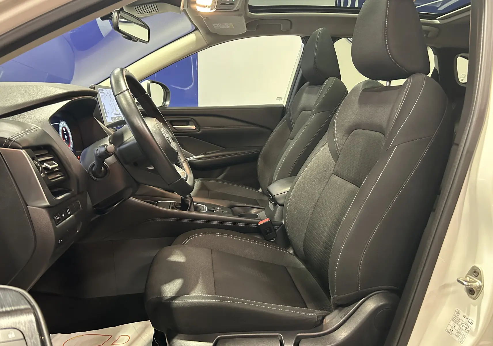 Vue intérieure côté conducteur du Nissan Qashqai blanc lunaire 2023, sièges tissu noir et volant cuir.