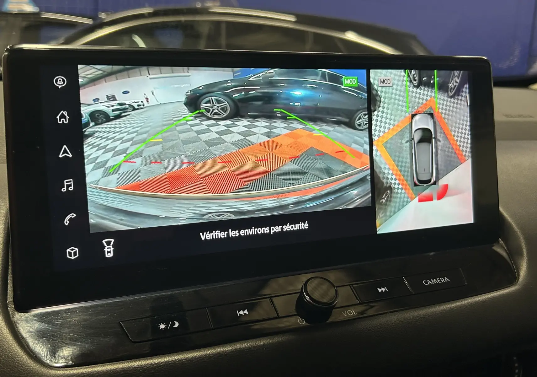 Écran de caméra 360° du Nissan Qashqai blanc lunaire, affichant vue arrière et vue aérienne du véhicule en parking.