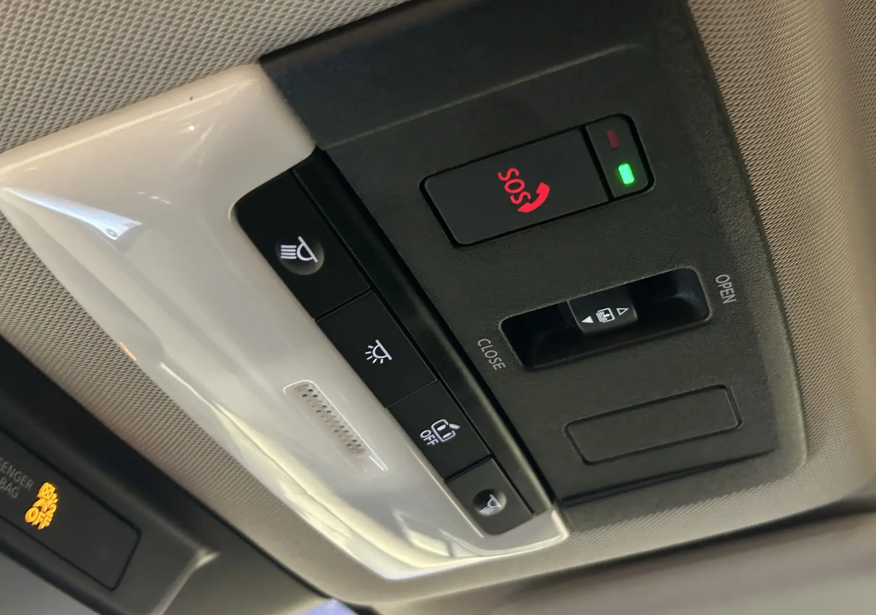 Vue en gros plan des commandes du toit panoramique et du bouton SOS dans l'habitacle du Nissan Qashqai blanc lunaire 2023.