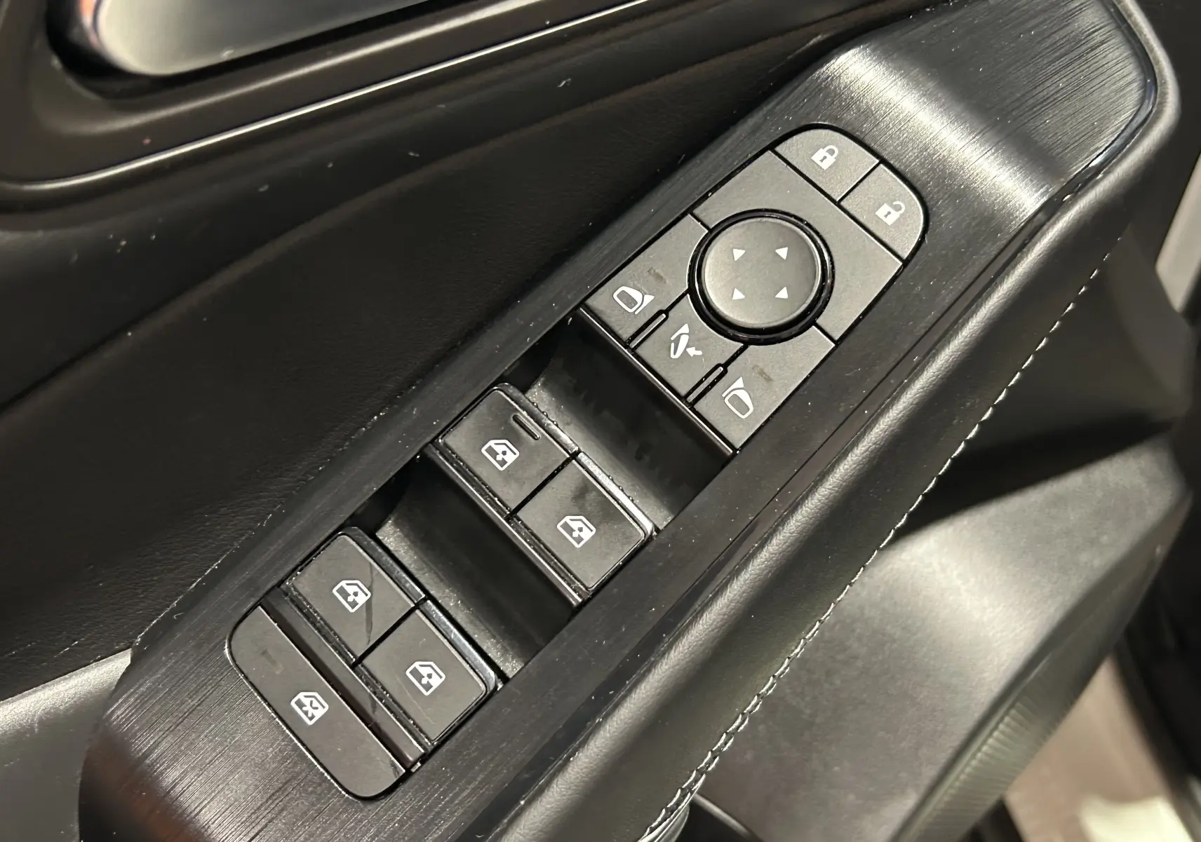 Gros plan sur les commandes des vitres et rétroviseurs côté conducteur du Nissan Qashqai 1.3 Hybrid 2023 en intérieur noir.
