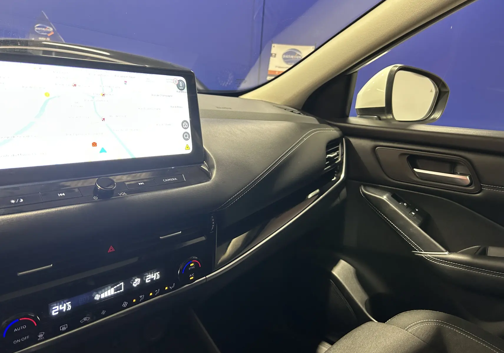 Vue intérieure côté passager du Nissan Qashqai blanc lunaire 2023, avec écran tactile et commandes climatisation visibles.