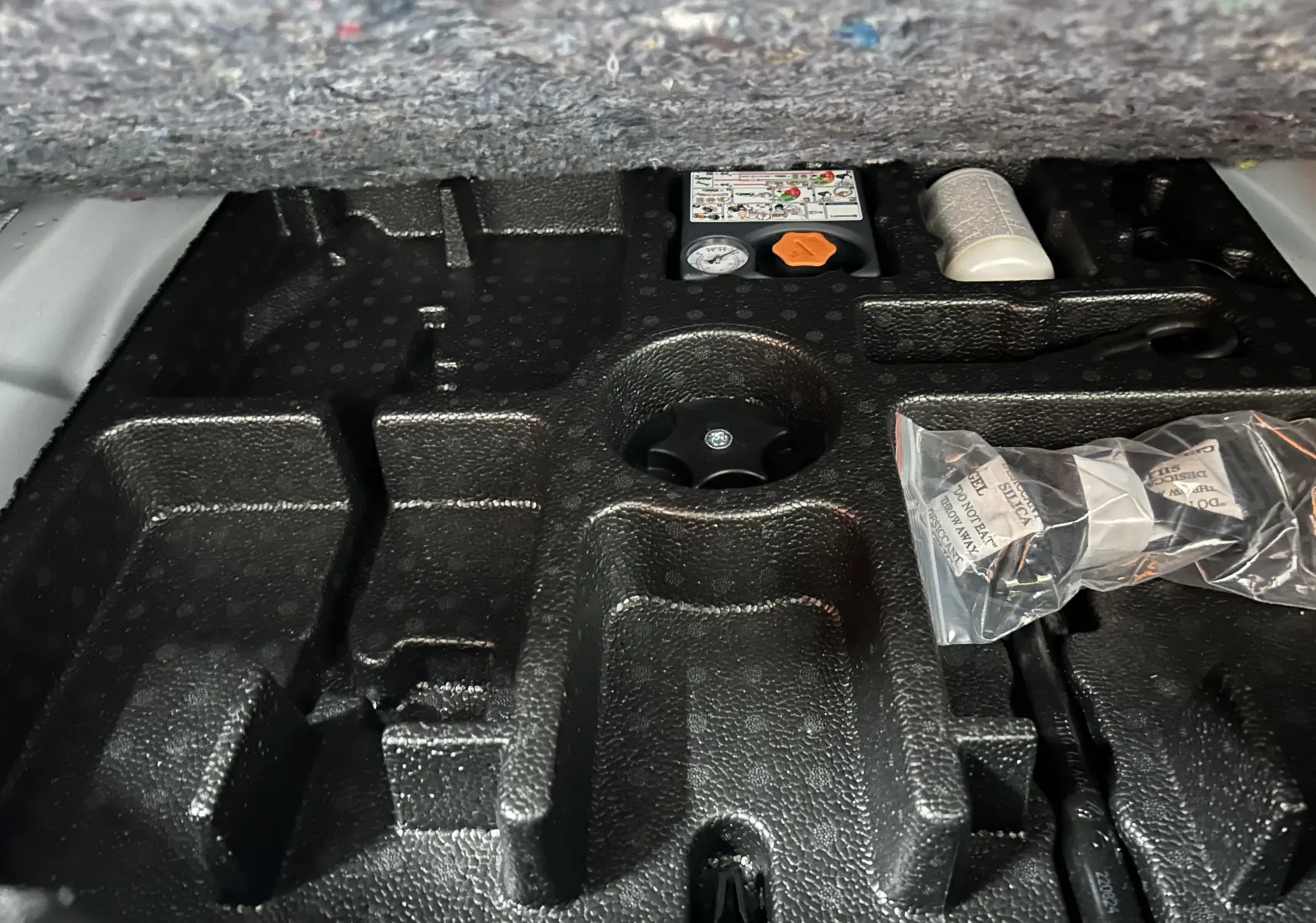 Gros plan sur le rangement en mousse noir sous le coffre du Nissan Qashqai blanc lunaire, avec accessoires et notice visibles.