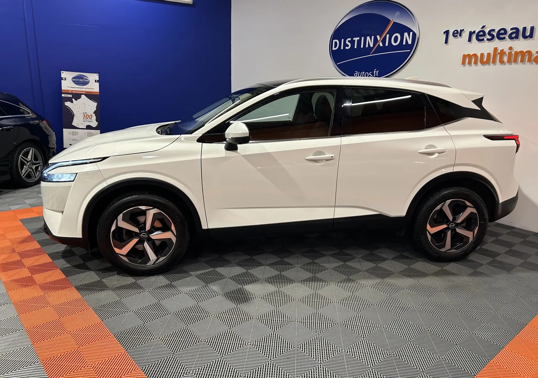 Profil côté gauche du Nissan Qashqai blanc lunaire 2023 en version 1.3 Hybrid N-Connecta, présenté en intérieur showroom.