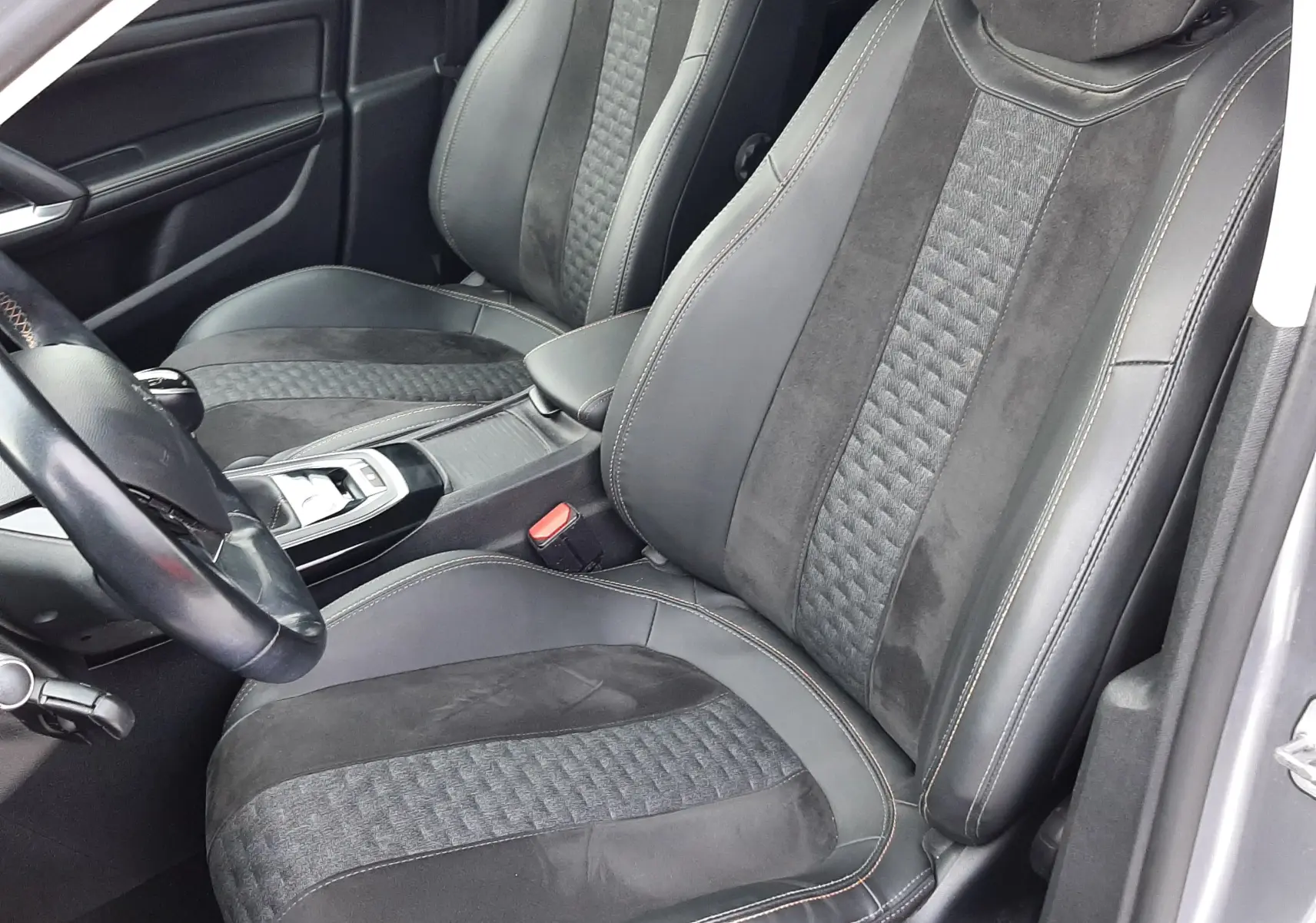 Vue intérieure de face des sièges avant en tissu noir et alcantara d'une Peugeot 308 SW gris Artense, avec coutures apparentes.