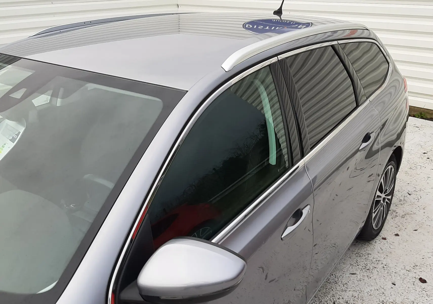 Vue 3/4 avant droit d'une Peugeot 308 SW gris Artense avec barres de toit et vitres teintées.