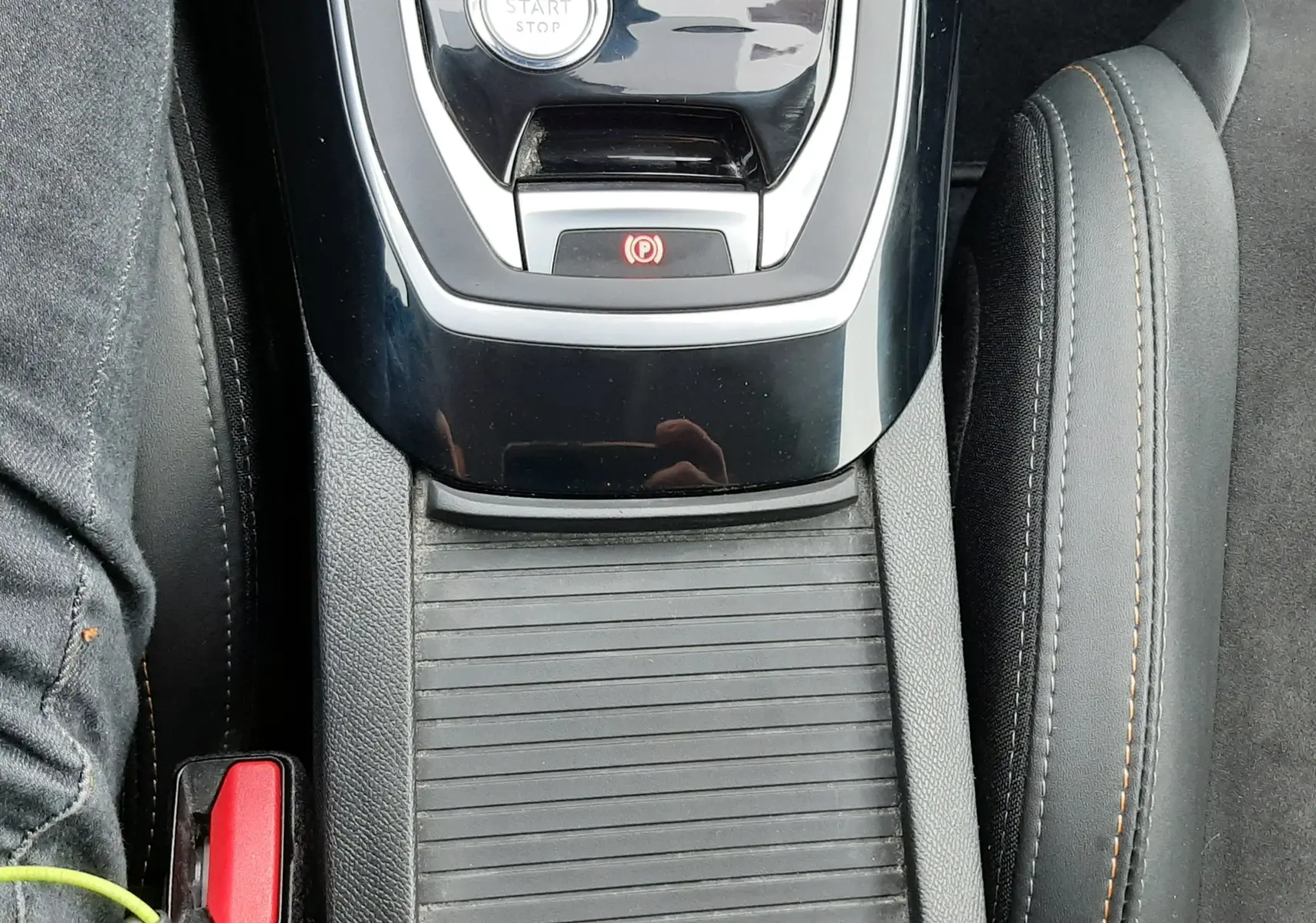 Vue plongeante sur la console centrale noire brillante de la Peugeot 308 SW 1.2 PureTech avec bouton start/stop et frein à main électronique.